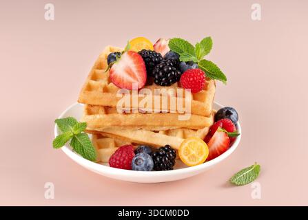 Pile de gaufres dorées garnies de baies fraîches et de feuilles de menthe sur une assiette blanche. Concept petit déjeuner ou brunch Banque D'Images