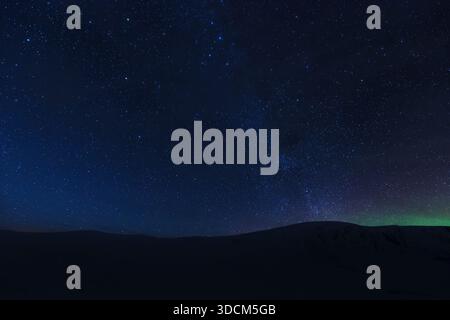 Un ciel nocturne clair et sombre rempli d'innombrables étoiles et un soupçon de la voie lactée ou de l'aurore, s'étend sur une chaîne de montagnes silhouettée ou un champ de neige A. Banque D'Images