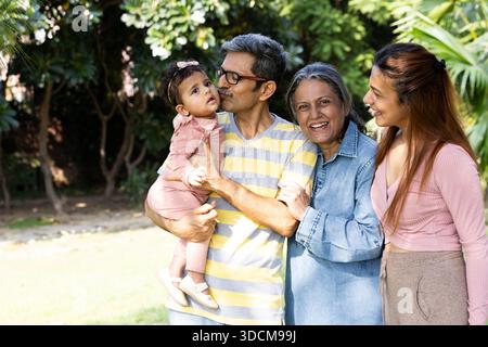 Heureuse famille indienne debout avec une petite fille à l'extérieur dans un parc verdoyant. Portrait lumineux de style de vie montrant l'amour, la convivialité et le multig Banque D'Images
