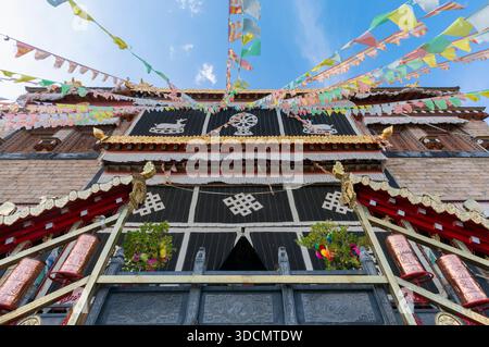 Architecture du monastère de Songzanlin avec des drapeaux de prière colorés flottant contre un ciel bleu clair. Banque D'Images