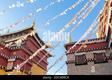 Architecture du monastère de Songzanlin avec des drapeaux de prière colorés flottant contre un ciel bleu clair. Banque D'Images