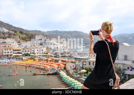 Visiteur photographiant le port et les parasols du village de Sant’Angelo depuis un point de vue élevé, Ischia, Campanie, Italie. Banque D'Images