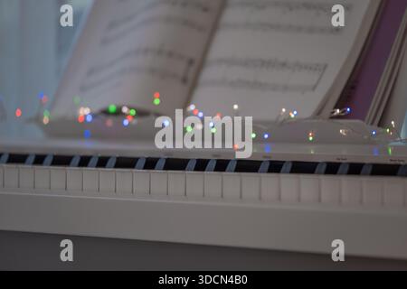 Gros plan d'un clavier de piano avec partitions ouvertes et lumières décoratives douces créant une atmosphère chaleureuse et créative. L'image transmet la pratique musicale Banque D'Images