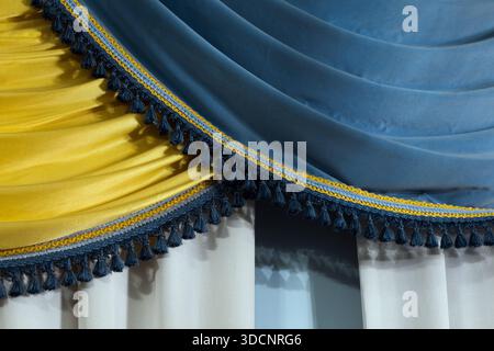 Gros plan de tissu bleu et jaune drapé avec frange de pompon bleu foncé, créant une scène de rideau cérémoniel et décoratif. Idéal pour scène ou vintage in Banque D'Images