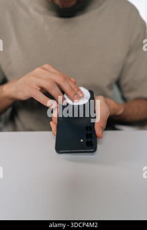 Plan vertical recadré d'un homme essuyant un smartphone avec un coton pour désinfecter et éliminer les germes. Concept d'hygiène, d'entretien des appareils et au quotidien Banque D'Images