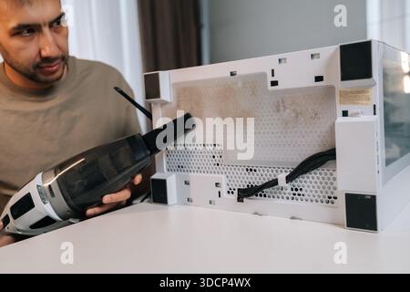 Homme concentré nettoyant l'unité du système informatique avec aspirateur, enlevant la poussière du filtre à air sale et du panneau de maille, fournissant l'entretien essentiel du pc Banque D'Images