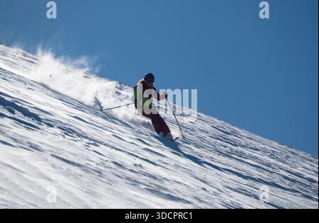 Une skieuse sculpte à travers la poudreuse fraîche sur une pente de montagne ensoleillée, dégageant la neige pendant qu'elle descend, créant un sport d'hiver dynamique et énergique Banque D'Images