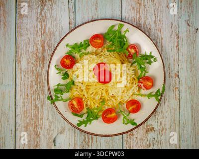 Vue de dessus de spaghetti avec parmesan râpé, feuilles de roquette et moitiés de tomates cerises disposées en cercle sur une plaque blanche au-dessus d'une table en bois rustique, Italie Banque D'Images