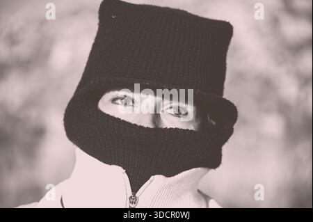 Portrait en gros plan d'une femme emballée dans des vêtements chauds d'hiver, portant un chapeau tricoté et un couvre-visage qui ne révèlent que ses yeux. Les tonalités douces et muettes Banque D'Images