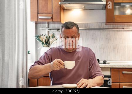 Homme adulte profitant d'une tasse de café à la table de la cuisine après le petit déjeuner fait maison. Routine matinale calme. Matin Home Cooking faire et manger petit déjeuner Banque D'Images