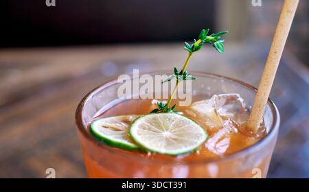 Un verre rafraîchissant de thé glacé au citron ou de thé à la pêche servi sur une table en bois dans un cadre de café. La boisson de couleur ambre est garnie de limette verte fraîche Banque D'Images