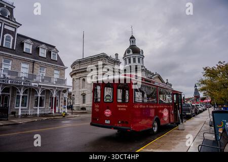 Un tramway rouge est stationné dans une rue humide à côté de l'hôtel de ville de Kingston et de l'hôtel Prince George tandis que des voitures bordent le trottoir sous un ciel couvert. KIN Banque D'Images
