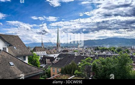 Vue de Zurich, Suisse, depuis Polyterrasse à l'université, clochers d'église, montagnes en arrière-plan, arbres au premier plan et nuages sur le ciel bleu Banque D'Images