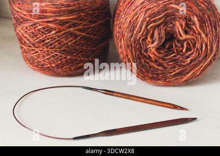 Fil marron chaud avec des aiguilles à tricoter en bois sur fond blanc. Aiguilles à tricoter et boules de fil orange. Boule et aiguilles de fil mérinos doux. Banque D'Images