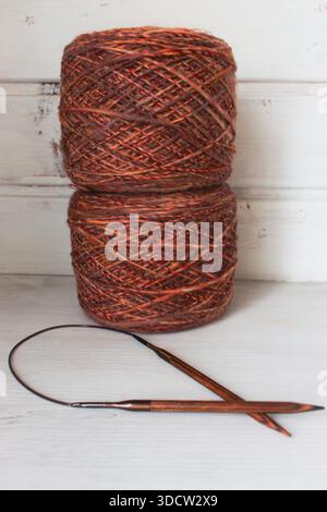 Fil marron chaud avec des aiguilles à tricoter en bois sur fond blanc. Aiguilles à tricoter et boules de fil orange. Boule et aiguilles de fil mérinos doux. Banque D'Images