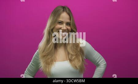 Femme se tient avec les mains sur les hanches dans un cadre de studio photo tout en souriant largement et regardant vers le haut ; confiance joie optimisme positivité. Banque D'Images