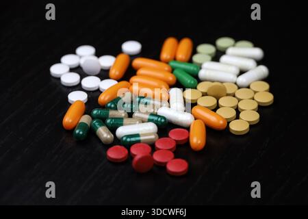 Pilules et capsules dispersées sur une table en bois noir. Contexte pour la pharmacie, les antibiotiques, les vitamines, les compléments alimentaires Banque D'Images