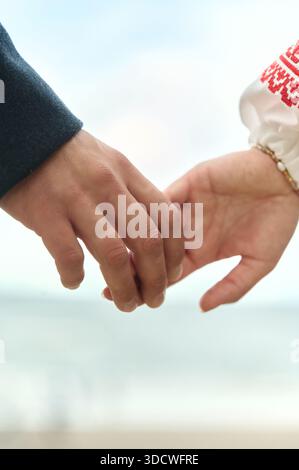 Un gros plan de deux personnes se rapprochant doucement des mains de l'autre près de la mer, capturant un moment tendre de connexion, d'amour et de convivialité avec Banque D'Images