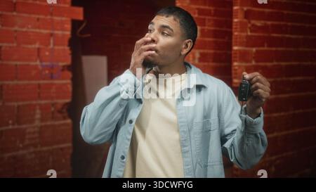 Homme tenant les clés de voiture et haussant les épaules dans la porte du bâtiment à côté du mur de briques ; incertitude d'hésitation occasionnelle. Banque D'Images