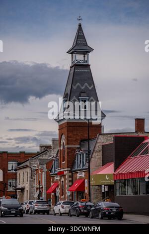 Une grande tour d'horloge en brique avec une flèche en ardoise s'élève au-dessus des devantures de magasins et des voitures garées dans une rue de la ville de Kingston, en Ontario. Kingston, Canada - mai 09, Banque D'Images