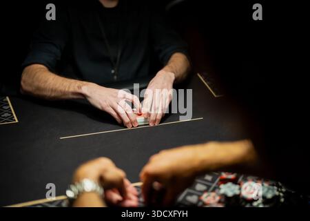 Scène de table de poker de casino en direct avec les mains du croupier organisant le jeu de cartes et les joueurs en attente de parier, montrant des procédures contrôlées dans l'industrie du jeu Banque D'Images