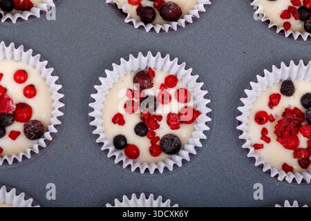 Les muffins aux baies non cuits dans une plaque de cuisson sont prêts à être cuits. Les muffins sont remplis de groseilles rouges, de framboises et de bleuets. Banque D'Images