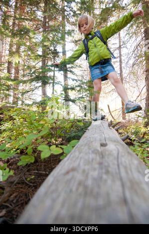 Une fille d'âge élémentaire se balance sur une bûche lors d'une randonnée dans le parc national de Grand Teton, Jackson Hole, Wyoming. Banque D'Images