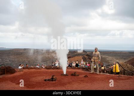 Groupe de touristes regardant un jet de vapeur comme l'eau est déversée dans des trous dans le sol, Timanfaya National Park, Lanzarote, îles Canaries, Espagne Banque D'Images