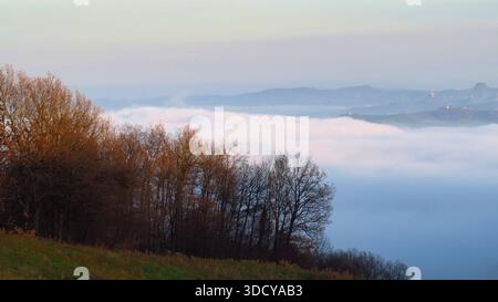 Une vue panoramique à couper le souffle d'une épaisse couche de nuages et de brouillard couvrant les vallées de Parme, en Italie. La lumière du coucher de soleil illumine les arbres d'automne Banque D'Images