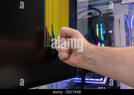 Gros plan d'une main avec un poing serré frappant un écran d'ordinateur, causant un motif de fissure dramatique avec des lignes verticales jaunes et multicolores, illu Banque D'Images