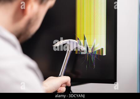 Gros plan d'une personne frappant un écran d'ordinateur noir avec un marteau, résultant en verre brisé et des lignes de pixels colorées et brisées, représentant des s numériques Banque D'Images