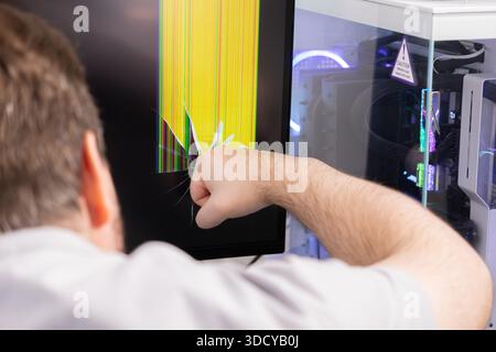 Gros plan du poing d'une personne en colère brisant un écran d'ordinateur, montrant un écran brisé avec des pixels jaunes déformés et colorés, symbolisant DIG Banque D'Images