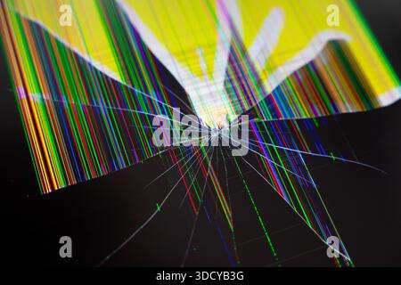 Vue détaillée d'un écran électronique cassé avec un point d'impact, présentant des motifs rayonnants et des lignes de pixels multicolores vives et corrompues, Banque D'Images