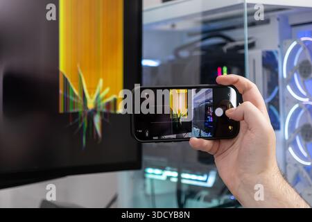 Gros plan d'une personne prenant une photo d'un écran de bureau défectueux montrant des lignes verticales jaunes distinctes et des dommages importants à l'écran Banque D'Images