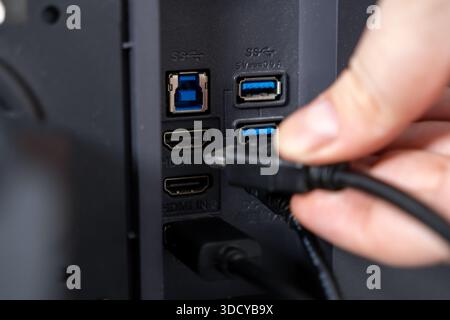 Gros plan de la main d'une personne branchant un câble HDMI noir dans le port HDMI IN 2 d'un appareil numérique, montrant la connexion moderne, l'installation du système Banque D'Images