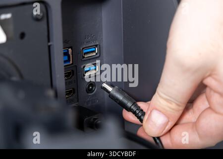 Gros plan de la main d'une personne insérant la fiche d'alimentation CC noire ronde dans le port arrière d'un gadget électronique sombre, mettant en évidence l'installation technique Banque D'Images