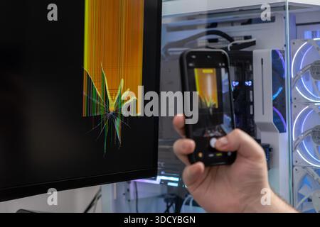 Gros plan de la main d'une personne à l'aide d'un smartphone pour capturer une image d'un écran d'ordinateur gravement brisé, mettant en évidence la défaillance d'un appareil technologique Banque D'Images