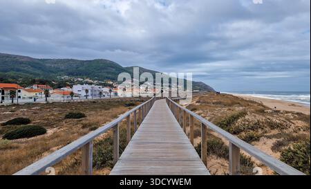 Promenade en bois s'étendant à travers les dunes de sable vers le village côtier de Quiaios niché contre des montagnes verdoyantes, avec le vaste océan Atlantique montré Banque D'Images