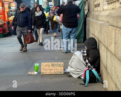 Une femme sans-abri est assise sur le trottoir le long de la 42e rue avec un panneau demandant de l'aide pour louer une chambre tandis que les piétons coulent par. Banque D'Images