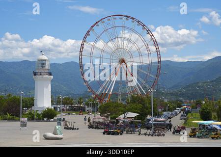 Grande roue et phare blanc avec des montagnes en arrière-plan sous le ciel bleu, parc d'attractions, Batumi, mer Noire, région d'Ajara, Adjara, AUTO Banque D'Images