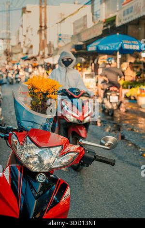 Ville de Duong Dong sur l'île de Phu Quoc. 19 décembre 2025. Une scène de marché de rue animée avec une personne portant un masque de protection et un sweat à capuche chevauchant un mot Banque D'Images