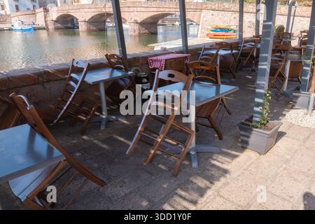 Une terrasse de café en plein air lumineuse avec des chaises simples disposées en plein soleil. La configuration propre et aérée convient au style de vie, à l'hospitalité et aux thèmes de voyage. Banque D'Images