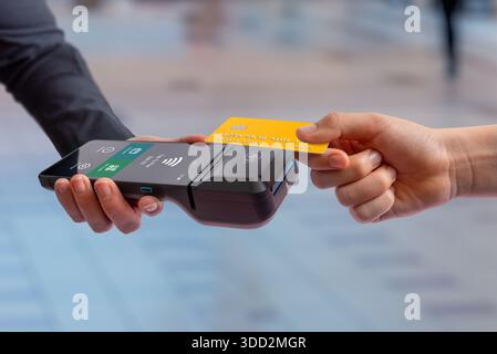 Le client insère une carte de paiement dans un terminal de point de vente mobile, illustrant le processus de paiement, la transaction au détail et l'expérience moderne de paiement par carte sans espèces Banque D'Images