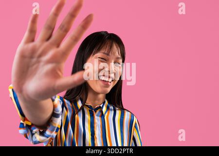 Beau portrait de femme chinoise sur fond coloré. Jeune femme asiatique faisant un geste d'arrêt avec sa main, souriant joyeusement. Portrait de tête activé Banque D'Images