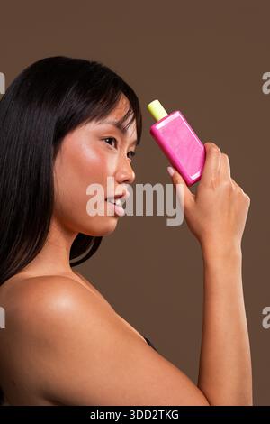 Beau portrait de femme chinoise sur fond coloré. Femme asiatique tenant un produit électronique personnel rose et vert citron. Elle se tourne vers le Banque D'Images