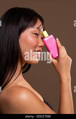 Beau portrait de femme chinoise sur fond coloré. Jeune femme asiatique souriante tenant un dispositif de vape jetable moderne, rose et jaune près de son f Banque D'Images