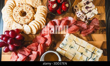 Belle planche de charcuterie avec salami, raisins, craquelins, assortiment de fromages, camembert cuit au four avec sauce aux fruits, fromage à la crème, poivrons farcis et miel Banque D'Images