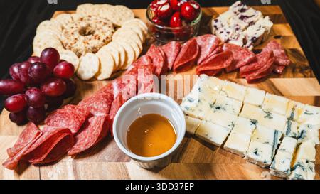 Belle planche de charcuterie avec salami, raisins, craquelins, assortiment de fromages, camembert cuit au four avec sauce aux fruits, fromage à la crème, poivrons farcis et miel Banque D'Images
