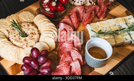 Belle planche de charcuterie avec salami, raisins, craquelins, assortiment de fromages, camembert cuit au four avec sauce aux fruits, fromage à la crème, poivrons farcis et miel Banque D'Images