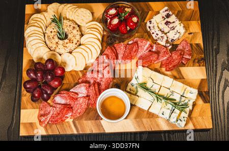 Belle planche de charcuterie avec salami, raisins, craquelins, assortiment de fromages, camembert cuit au four avec sauce aux fruits, fromage à la crème, poivrons farcis et miel Banque D'Images